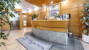 Un mostrador de recepción de hotel con encimera de madera, una zona de recepción, un refrigerador y una planta en maceta.
