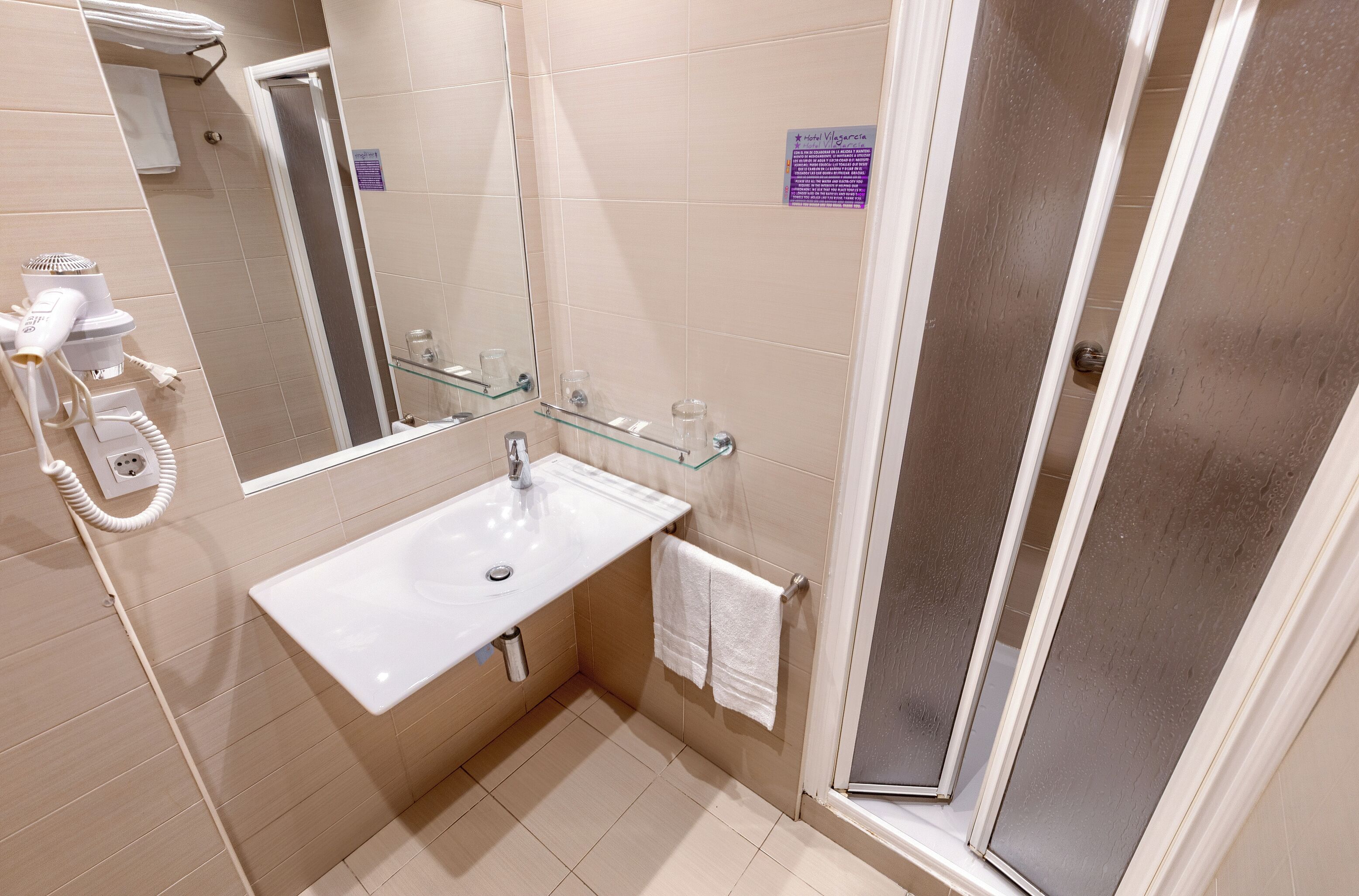 A bathroom with a sink, mirror, towel rack, and a glass shower enclosure.
