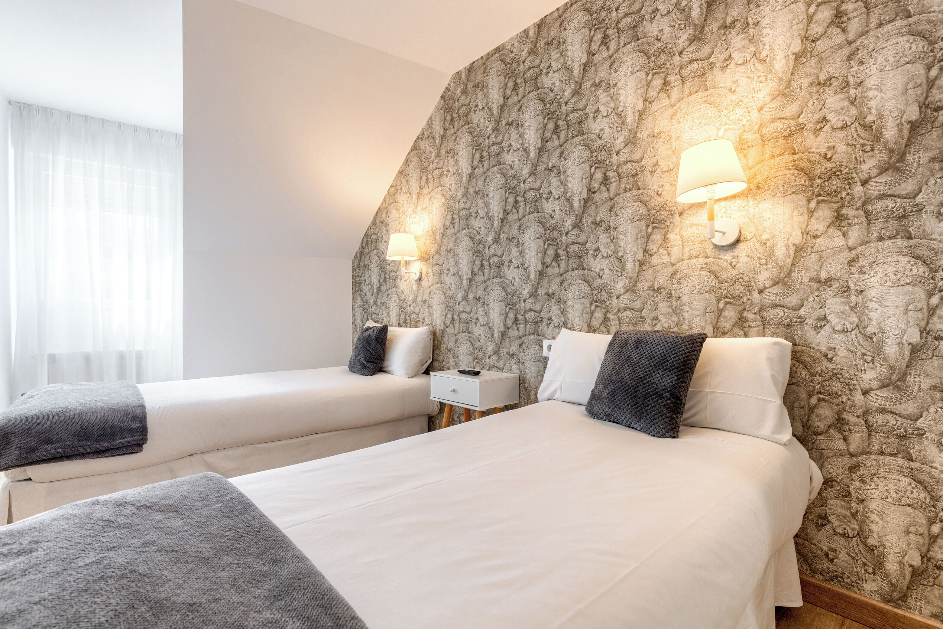 A hotel room with two beds, a nightstand, a lamp, and a patterned wall.