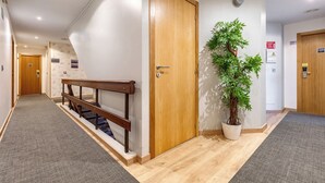 Un pasillo con puerta de madera, escalera con barandilla de madera, planta en maceta y piso alfombrado.