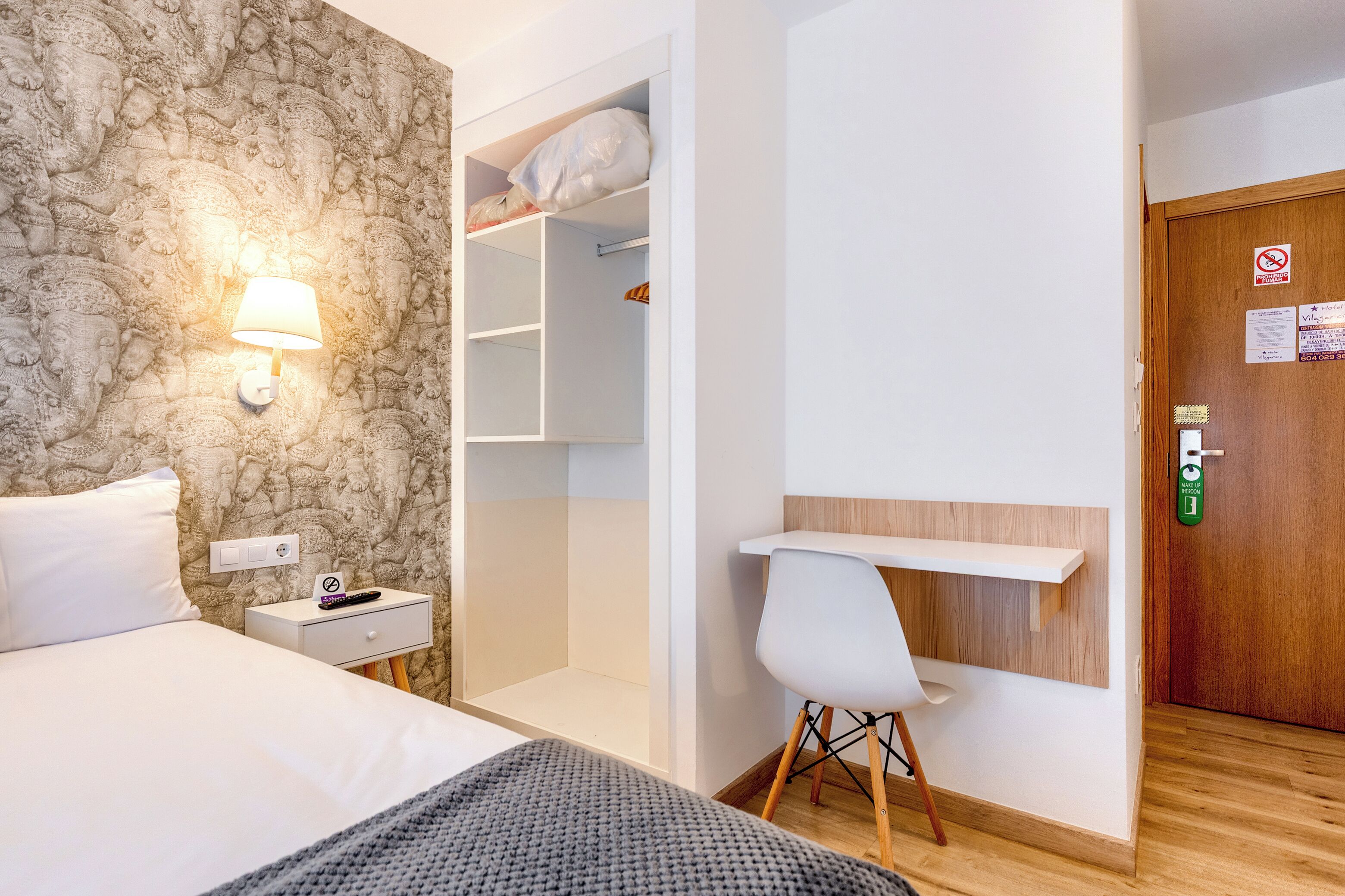 Habitación de hotel con cama, mesita de noche, escritorio con silla, armario y pared con diseño de piedra.