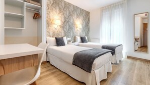 Habitación de hotel con dos camas, un escritorio, una silla y un armario.
