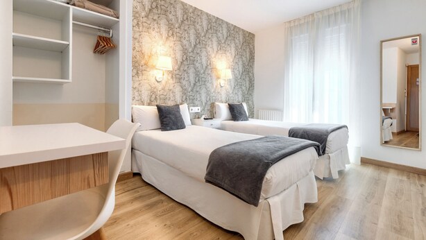 Habitación de hotel con dos camas, un escritorio, una silla y un armario.
