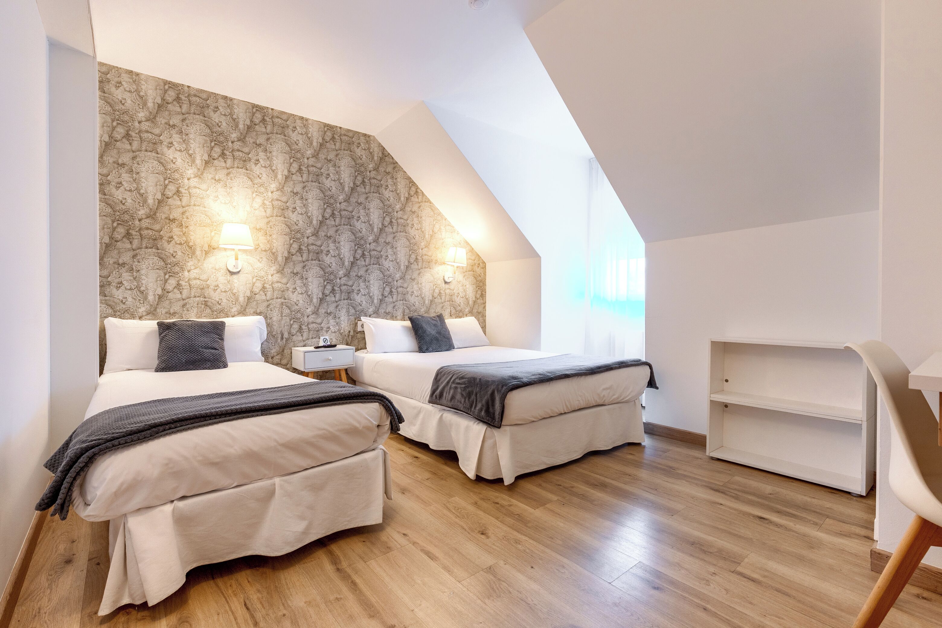 A modern bedroom with two beds, a stone accent wall, and a skylight.