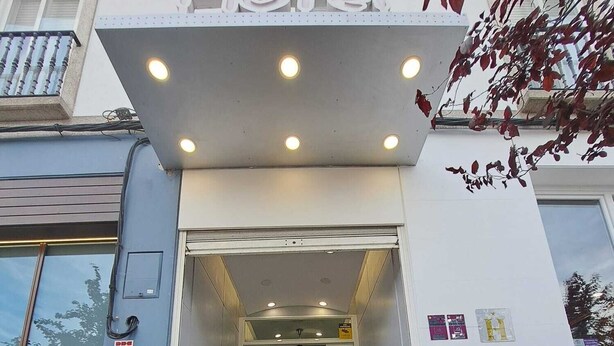 Entrada de un hotel con una escalera que lleva al vestíbulo, un mostrador de recepción y un cartel con el nombre del hotel.