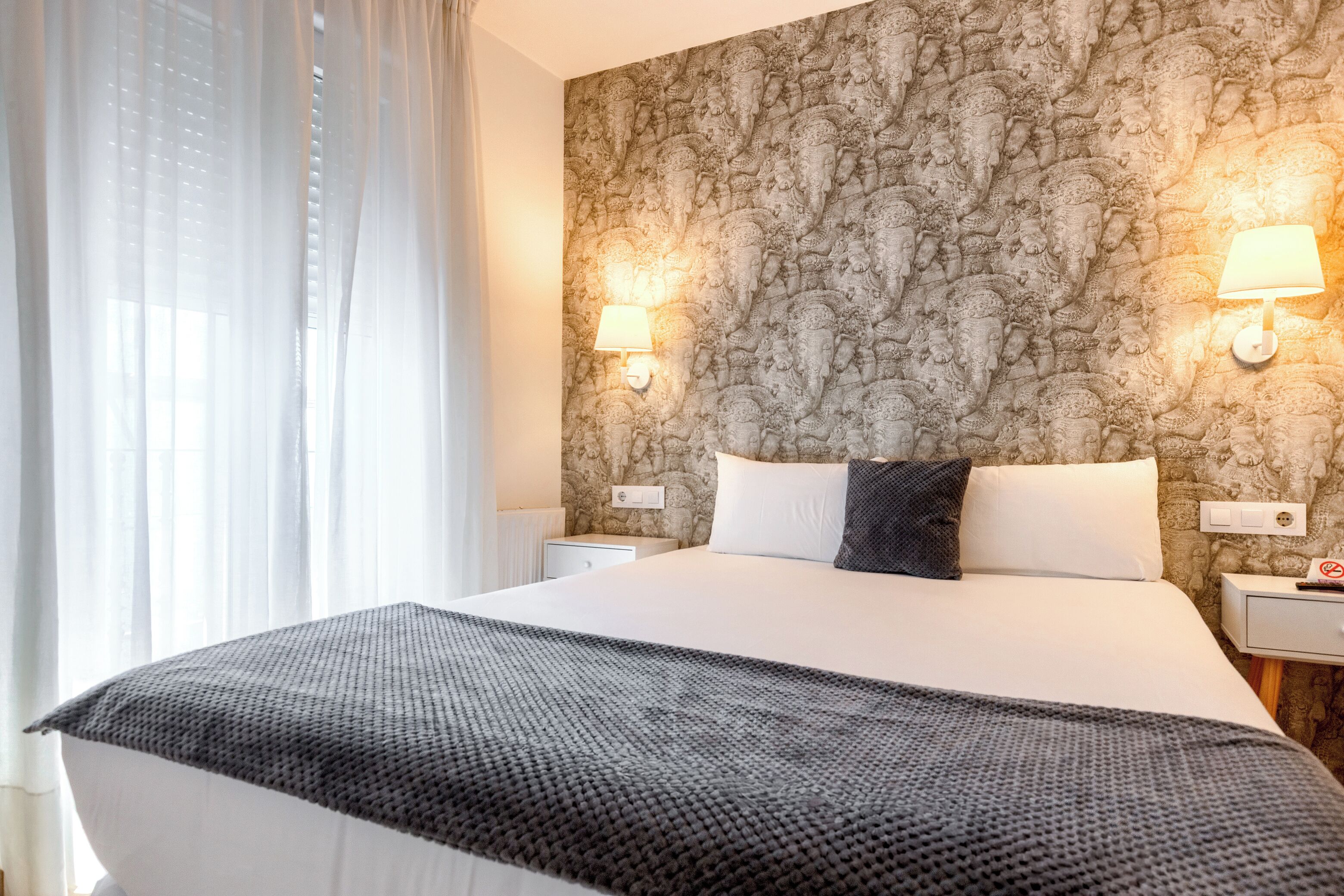 A hotel room with a large bed, two bedside lamps, a nightstand, and a patterned wall.