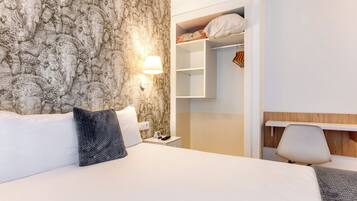 A hotel room with a bed, a nightstand, a lamp, a wardrobe, and a chair.