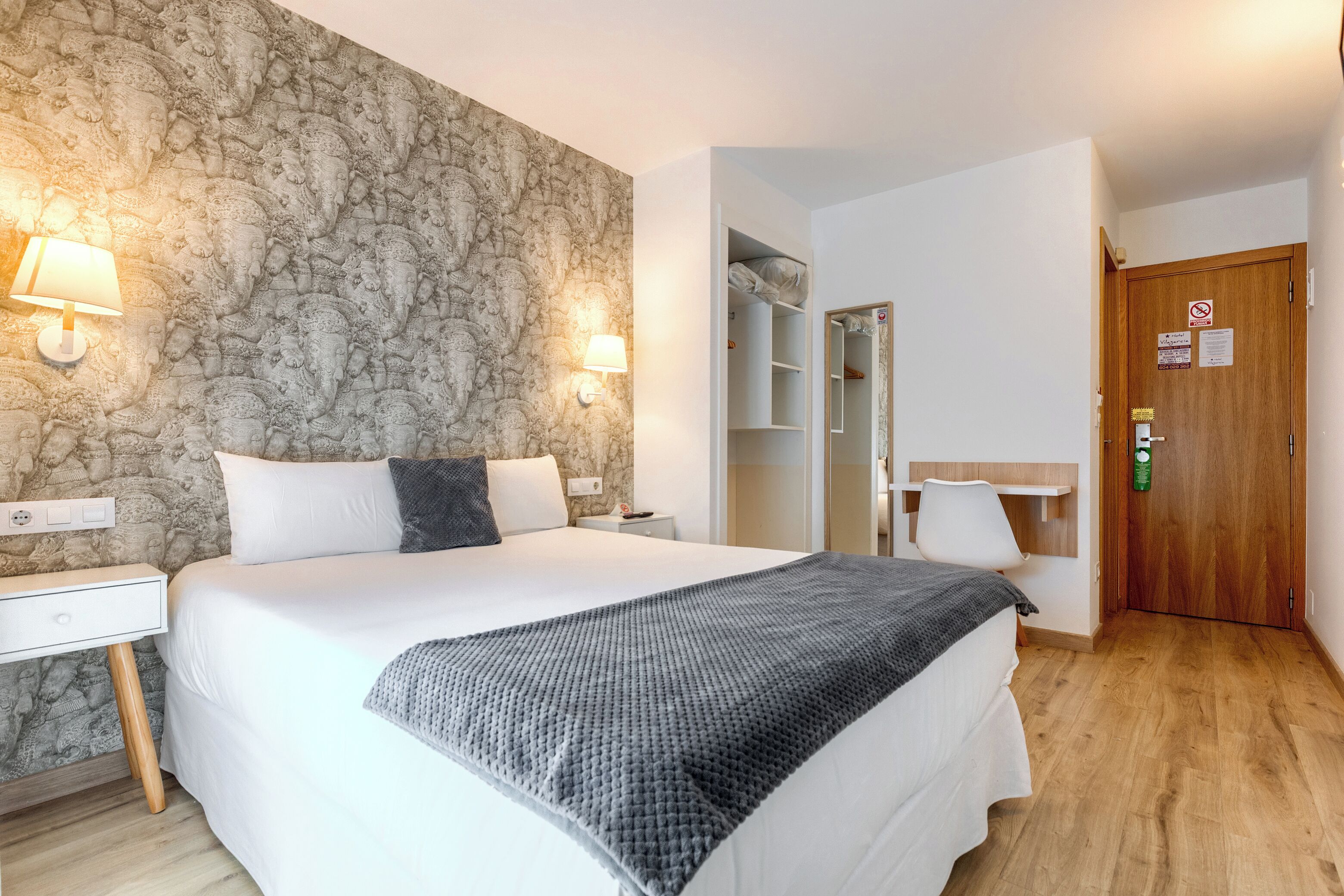 A bedroom with a large bed, bedside lamps, a wardrobe, and a door with a sign.