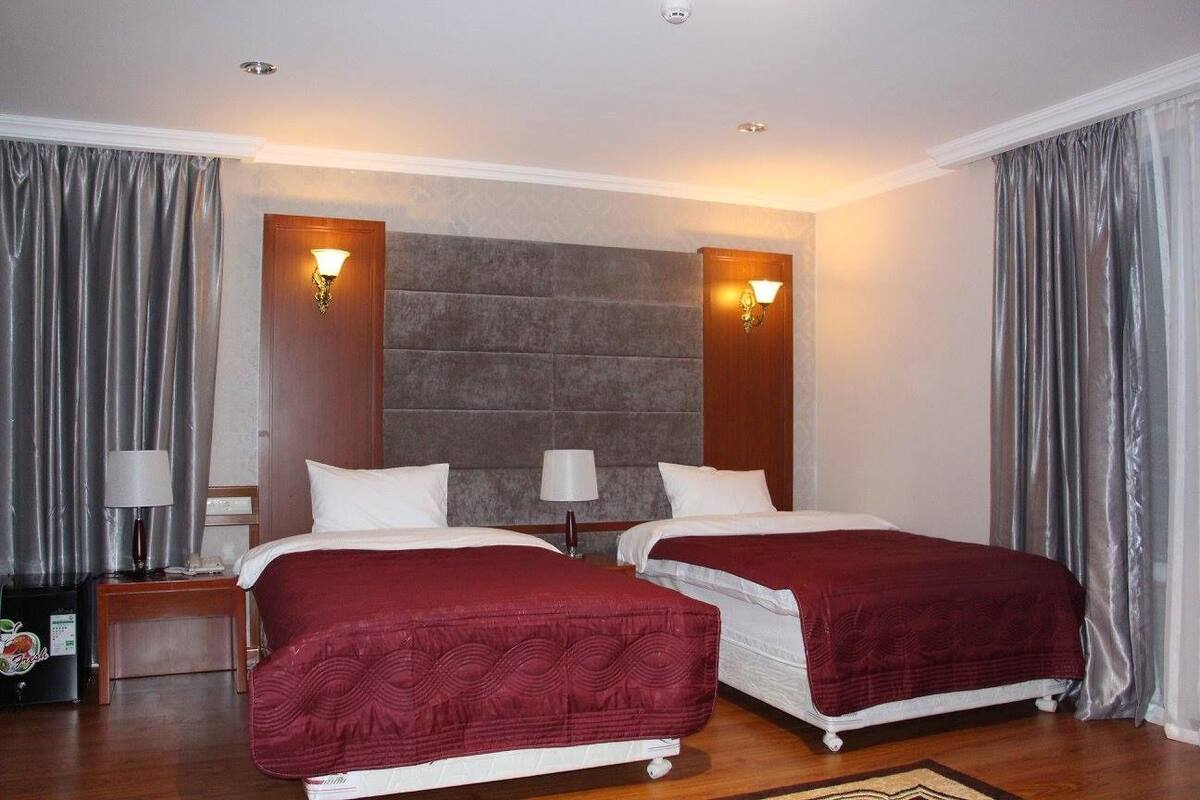 Habitación de hotel con dos camas, cada una con cubrecama rojo, cabecero de madera y dos lámparas de pared.