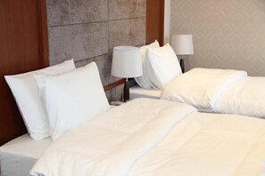 A hotel room with two beds, each with white linens and pillows, a wooden headboard, and a nightstand with a lamp. - Hotel Park Green (Poti)