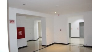 A clean, empty hallway with white walls and a polished floor. There are emergency exit signs and a fire safety poster on the wall. - Hotel Park Green (Poti)