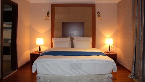 A hotel room with a large bed, two bedside lamps, a wooden headboard, and a nightstand with a lamp. - Hotel Park Green (Poti)