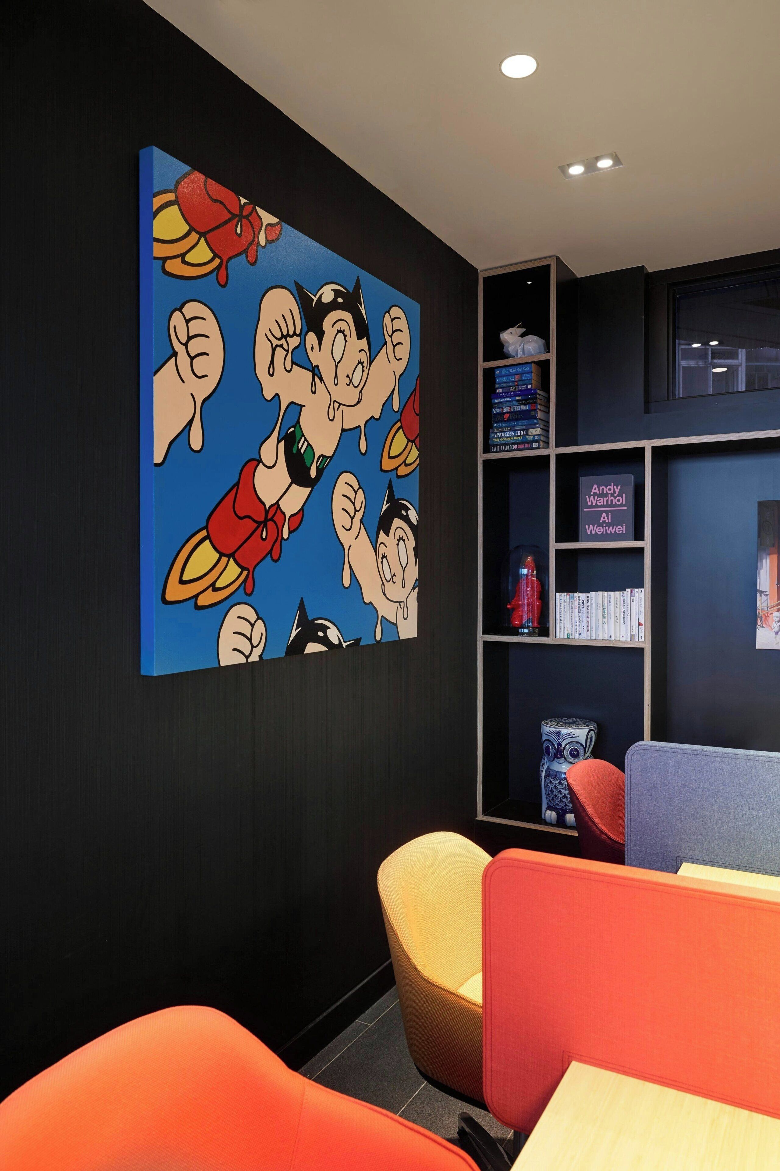 A modern office space with a large cartoon-themed wall art, a bookshelf with books and decorative items, and colorful seating areas.
