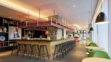 A modern bar area with high stools, a counter with bottles, and a seating area with round tables and chairs.