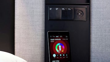 A control panel with a smartphone displaying room controls, a power outlet, and a red button.