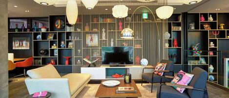 Una sala de estar moderna con un sofá, sillones, una mesa de centro y un televisor. Hay estanterías con diversos objetos y elementos decorativos.