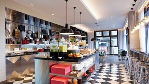 A modern kitchen with stainless steel appliances, a checkered floor, and a buffet area with various food items and utensils. - citizenM Taipei North Gate (Taipei)