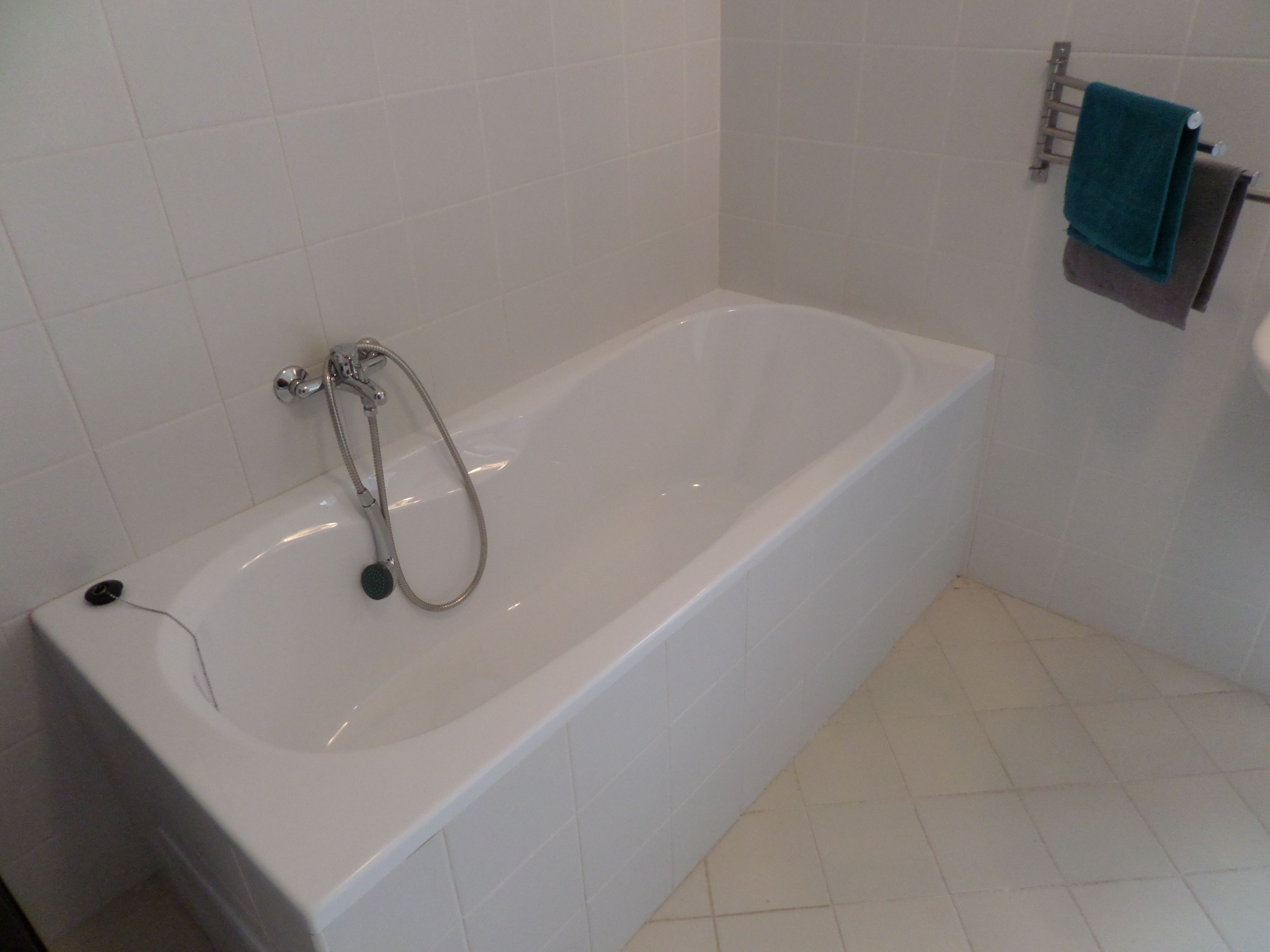 A white bathtub with a handheld showerhead, a towel rack with a blue towel, and a white sink.