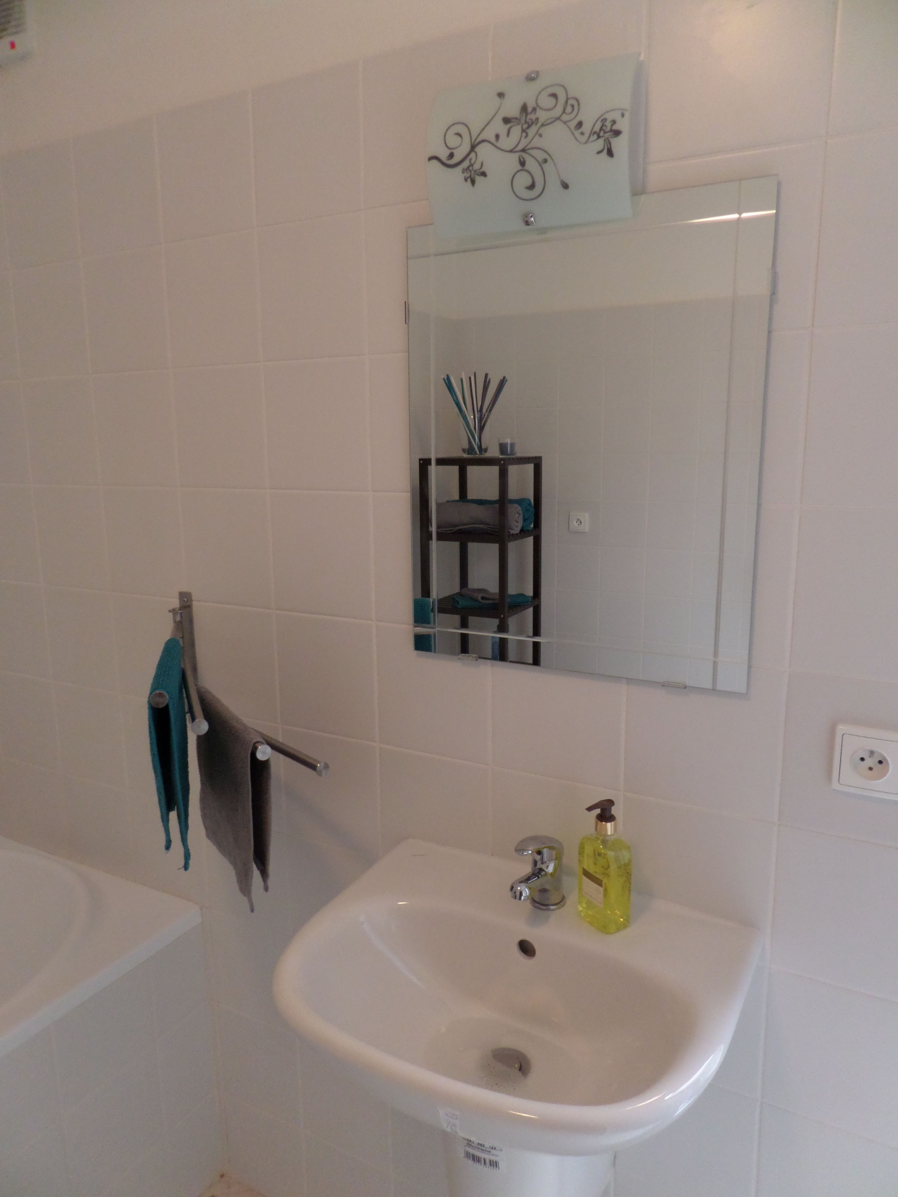 A bathroom with a white sink, a mirror, and a shelf with toiletries.