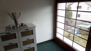 Una habitación con un amplio ventanal, un aparador blanco con cajones de mimbre y vistas a una zona residencial.