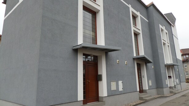 Un edificio moderno con fachada gris, detalles blancos y una puerta marrón.