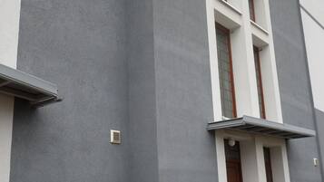 A modern building with a grey facade, a central entrance with a wooden door, and a small set of steps leading up to the entrance.