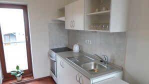 Una cocina con gabinetes blancos, un lavamanos de acero inoxidable y una planta en maceta cerca de la puerta.