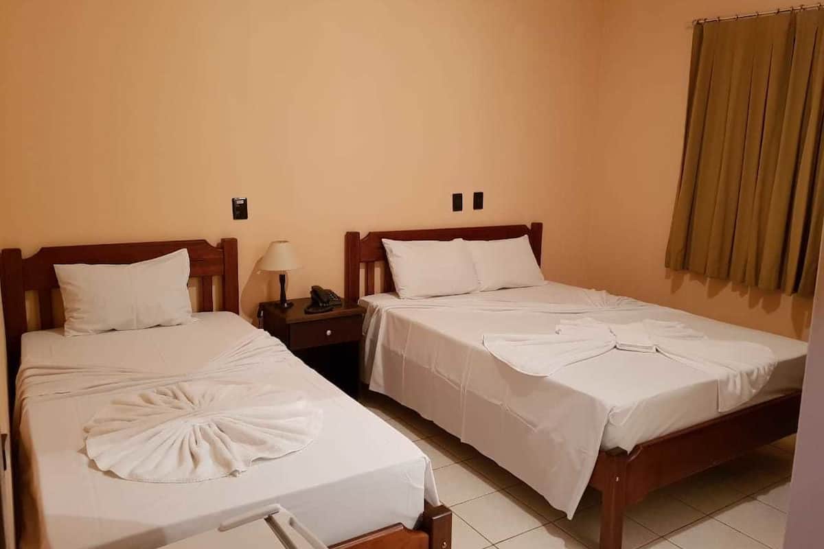 Habitación de hotel con dos camas individuales, una mesita de noche con lámpara y una ventana con cortinas.