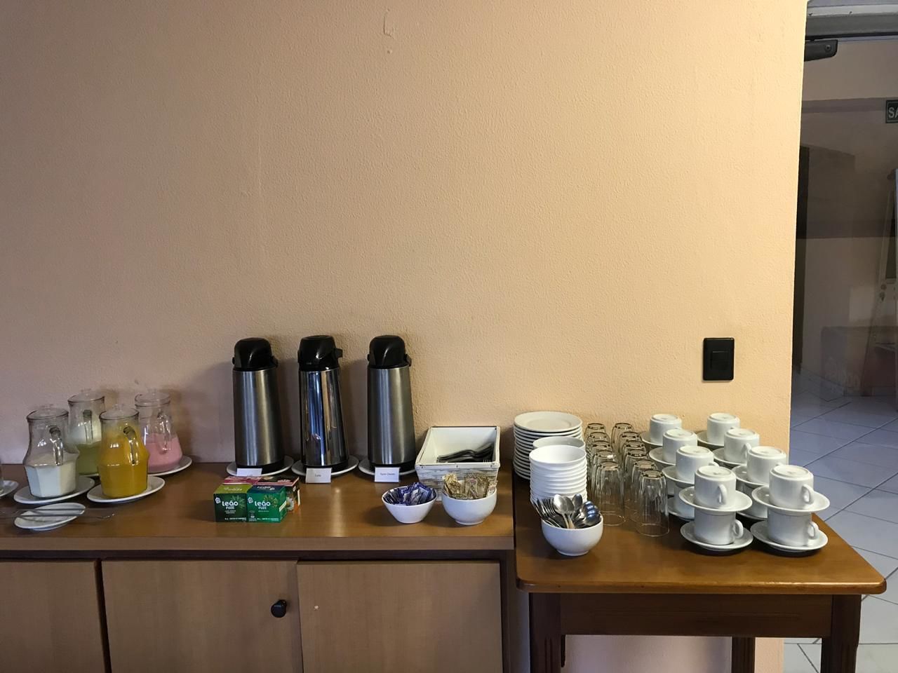 A breakfast buffet setup with various food and drink options, including coffee makers, tea, and a variety of dishes and utensils.
