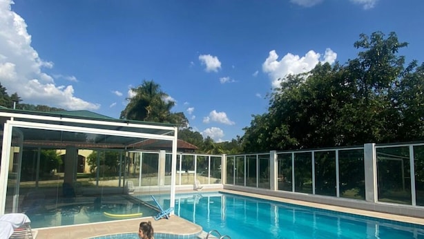 Une piscine avec un jacuzzi, le tout entouré d’une structure en verre, sous un ciel bleu dégagé.