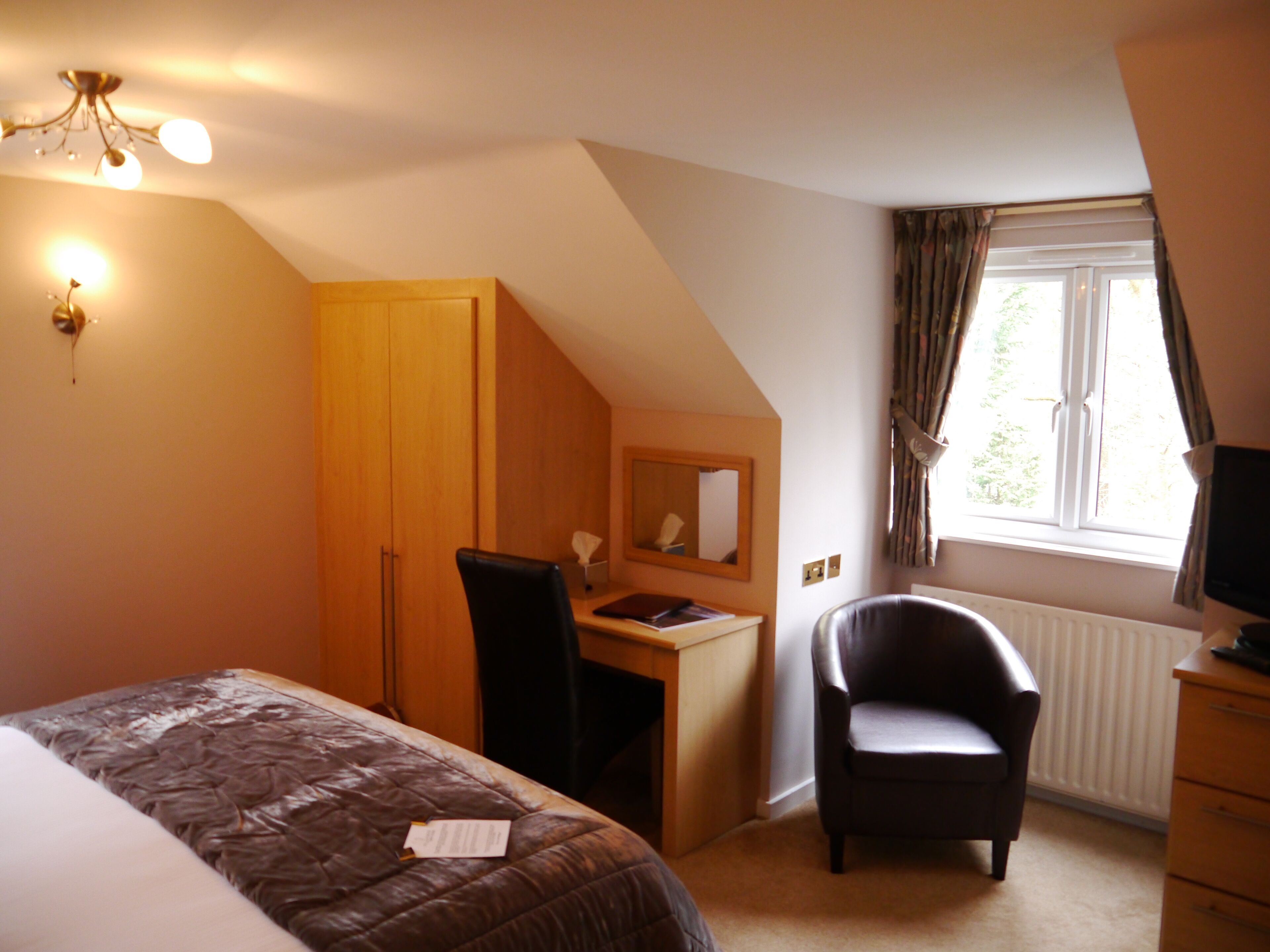 A bedroom with a bed, desk, chair, and a window with curtains.