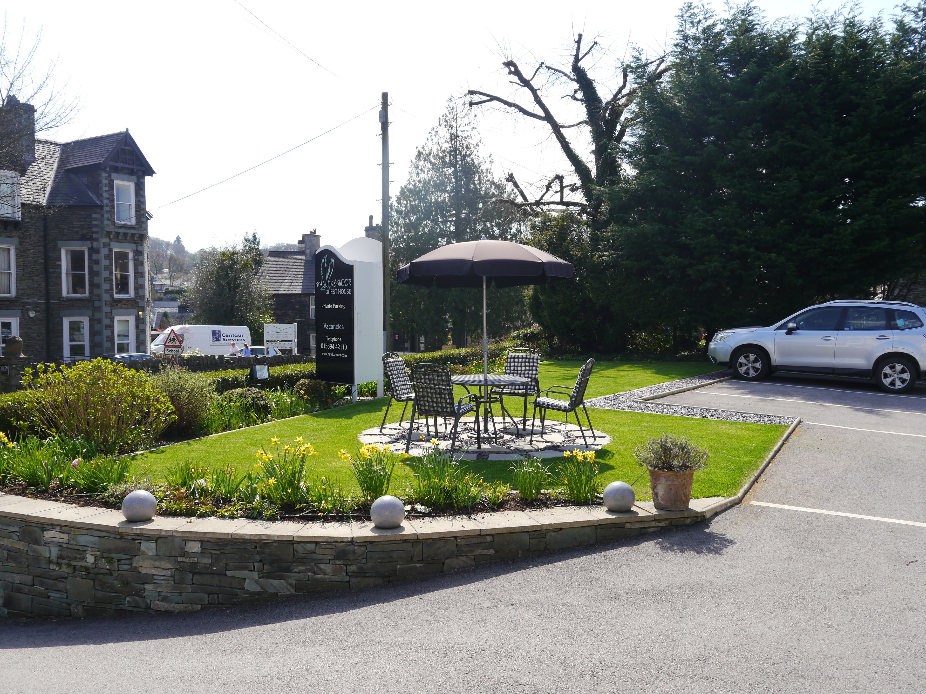 A guest house with a signboard, outdoor seating, and a parking area.