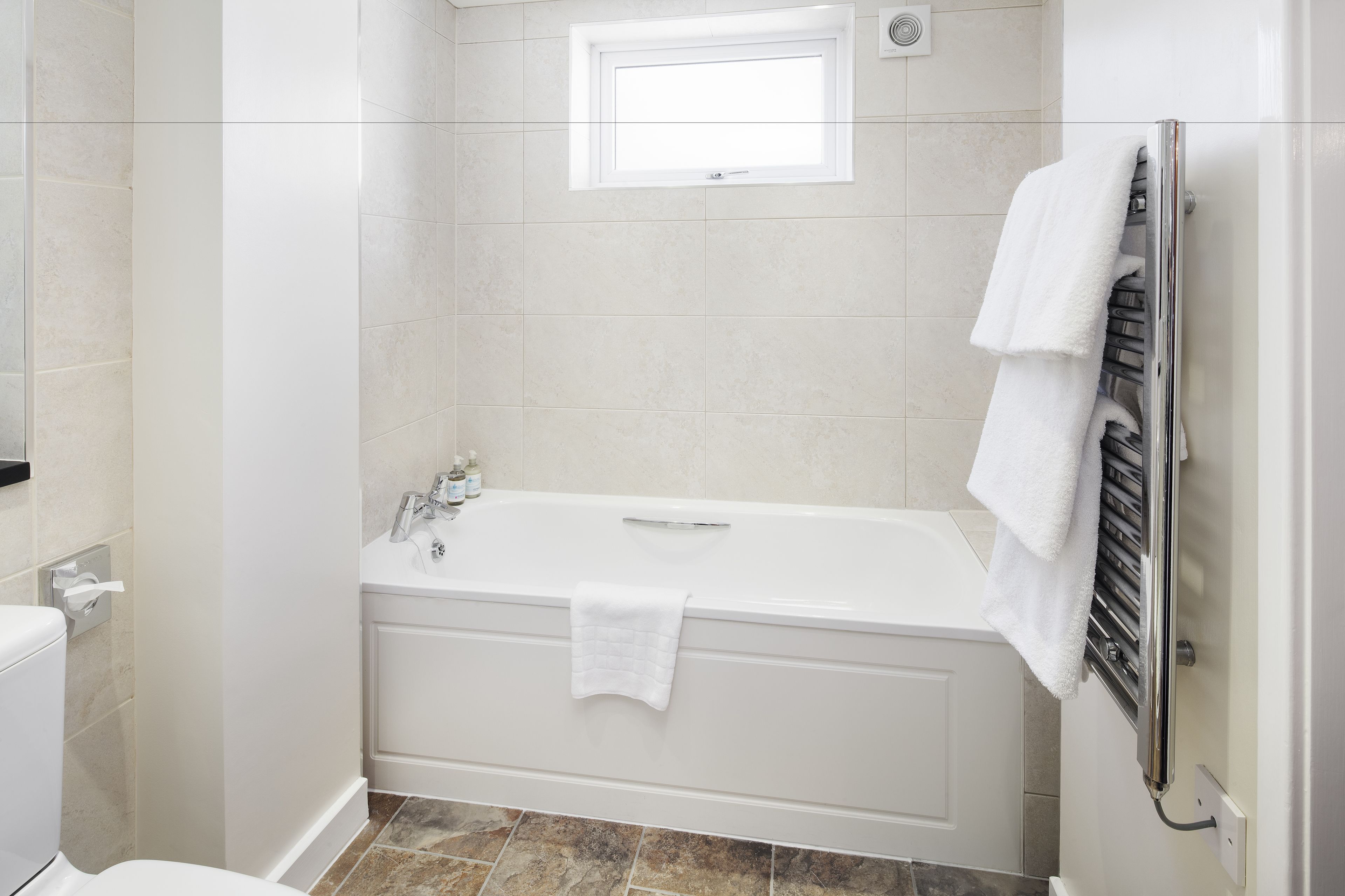 Une salle de bain moderne avec une baignoire blanche, une fenêtre au-dessus et un porte-serviettes avec des serviettes.