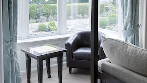 A hotel room with a large window, a black leather chair, a grey sofa, and two white towels on the bed.
