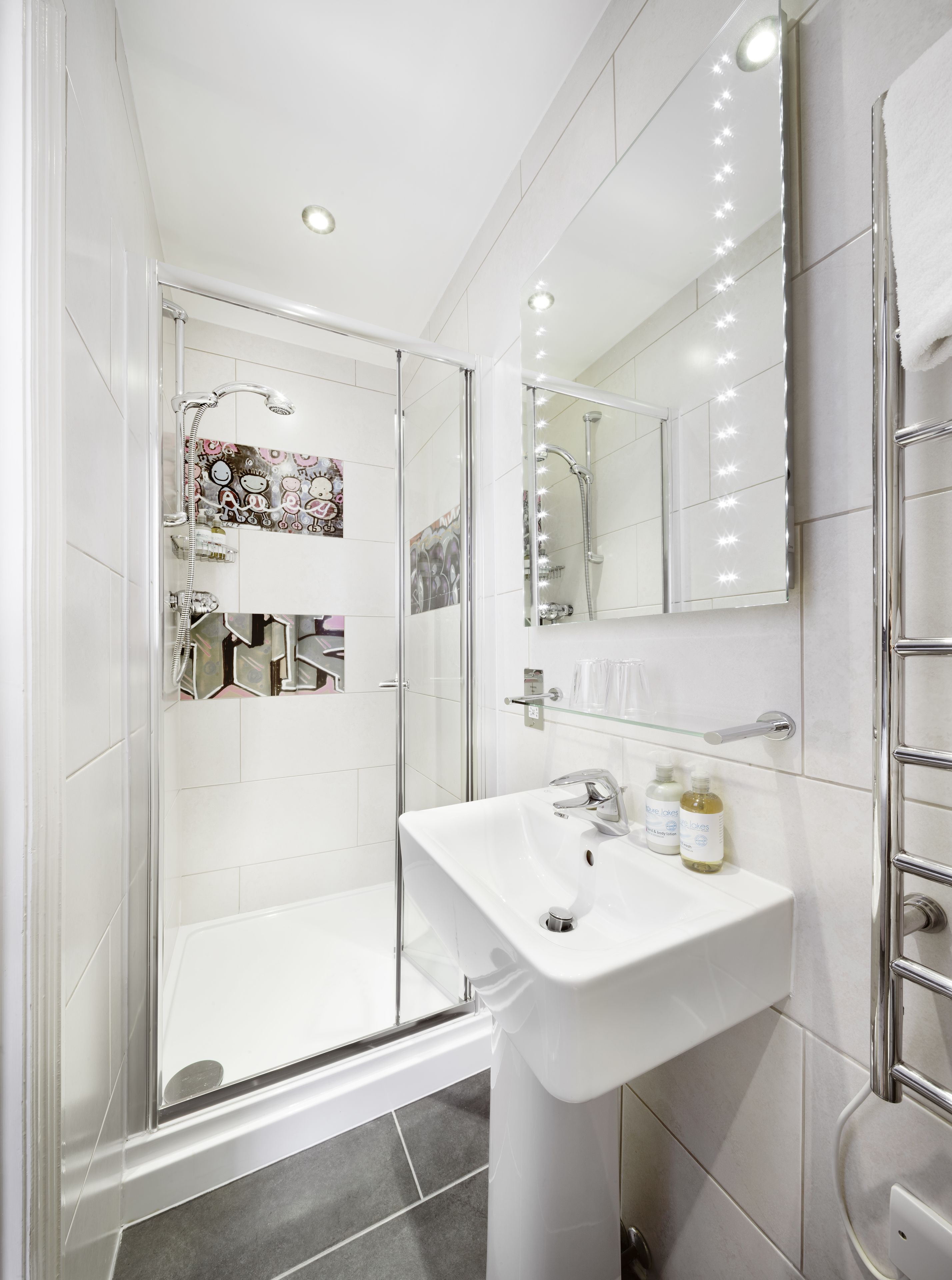 Une salle de bain moderne avec une douche à parois de verre, un lavabo blanc avec un miroir et un meuble-lavabo avec des articles de toilette.