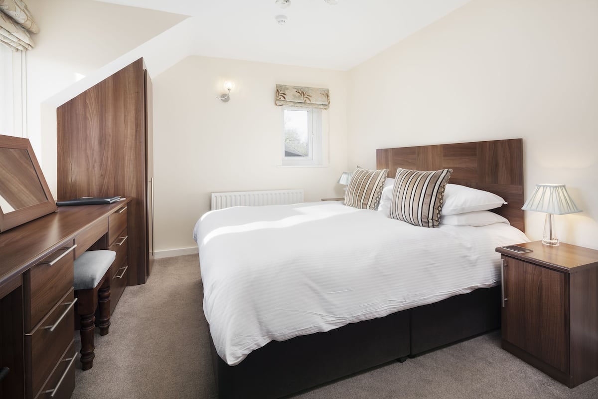 A bedroom with a large bed, wooden nightstands, a desk, and a wardrobe.