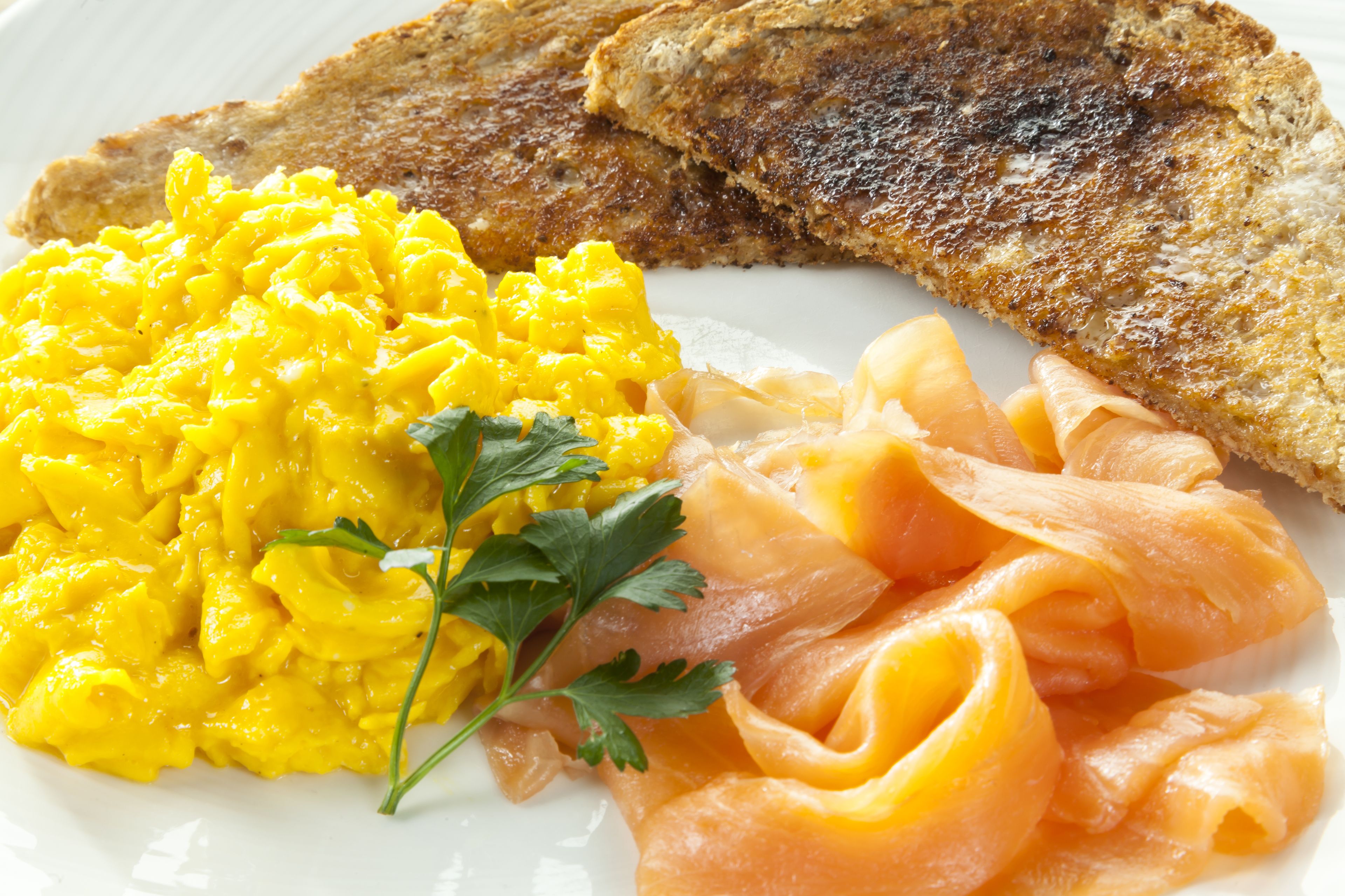 Scrambled eggs, smoked salmon, and toasted bread on a plate.