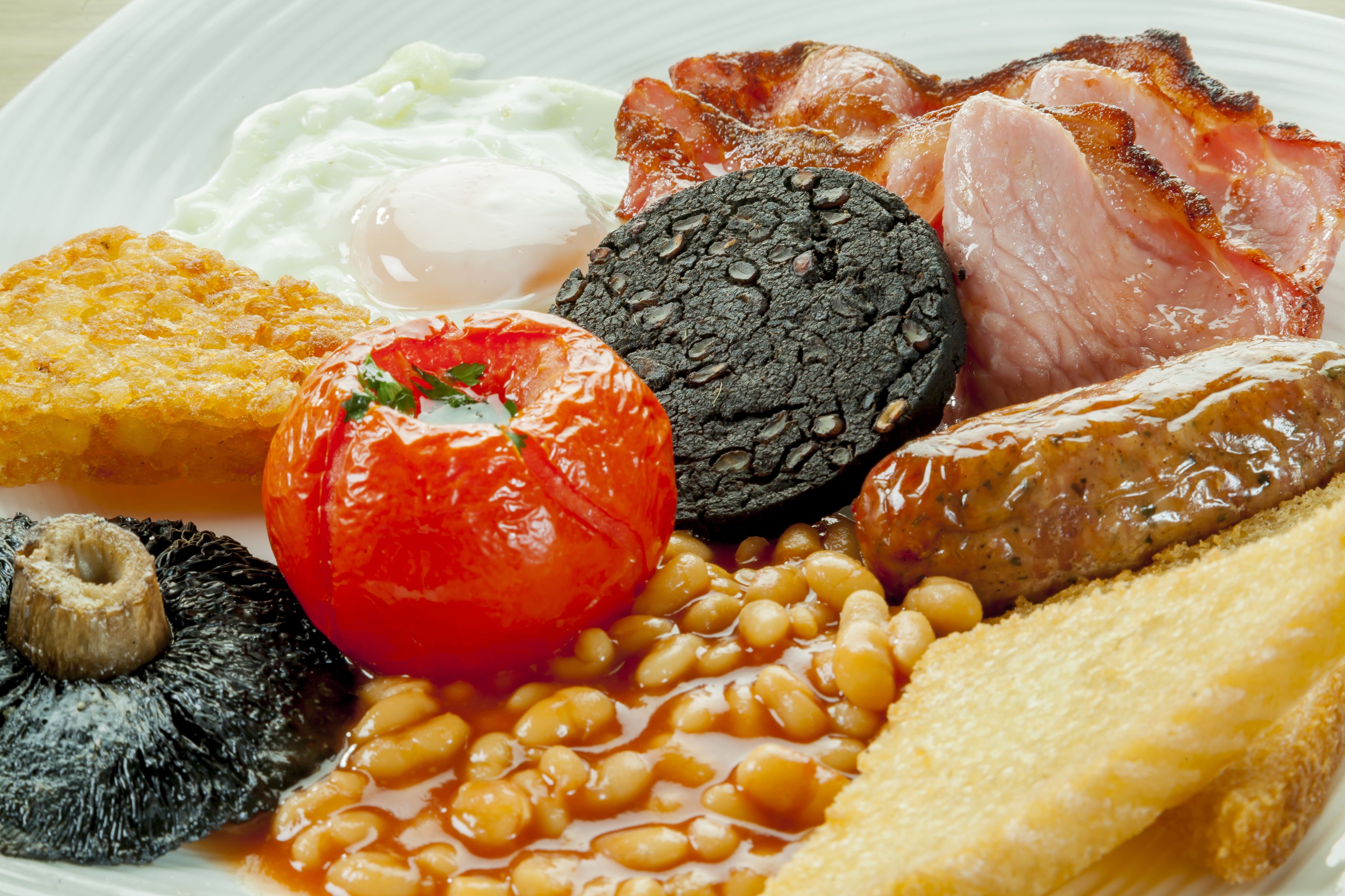 A plate of breakfast food including eggs, bacon, sausages, beans, toast, and a tomato.