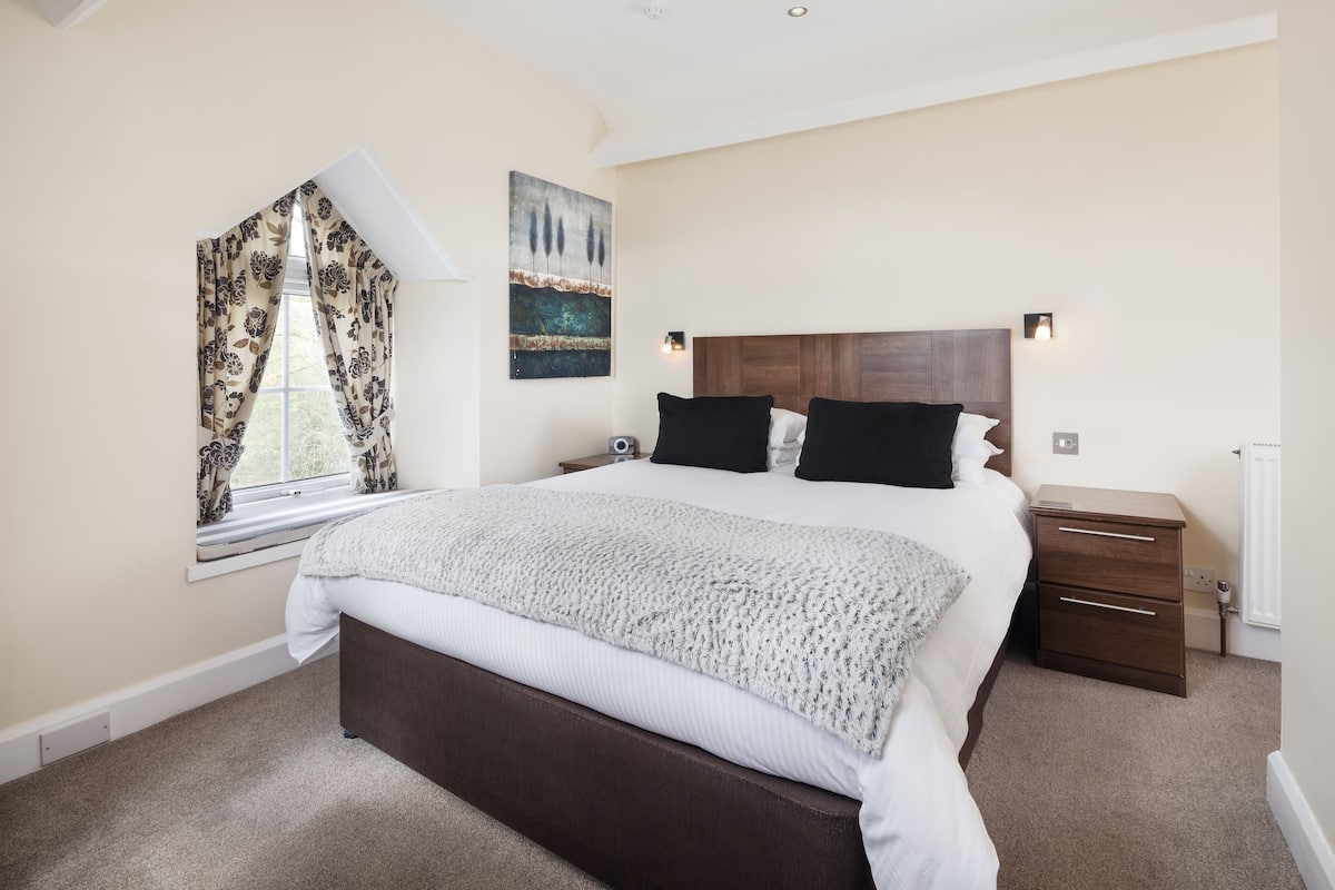 A bedroom with a large bed, a nightstand, a window with curtains, and a wall painting.