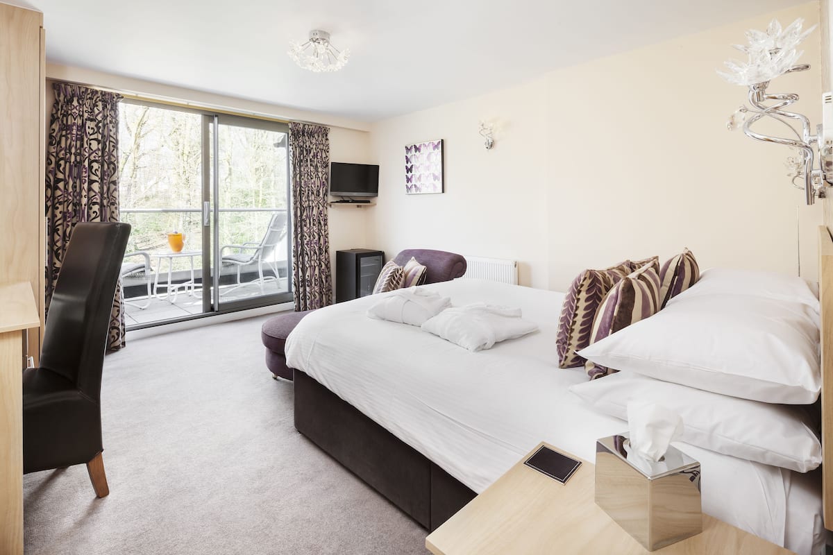 A hotel room with a bed, a desk, a chair, a TV, and a balcony with a table and chairs.