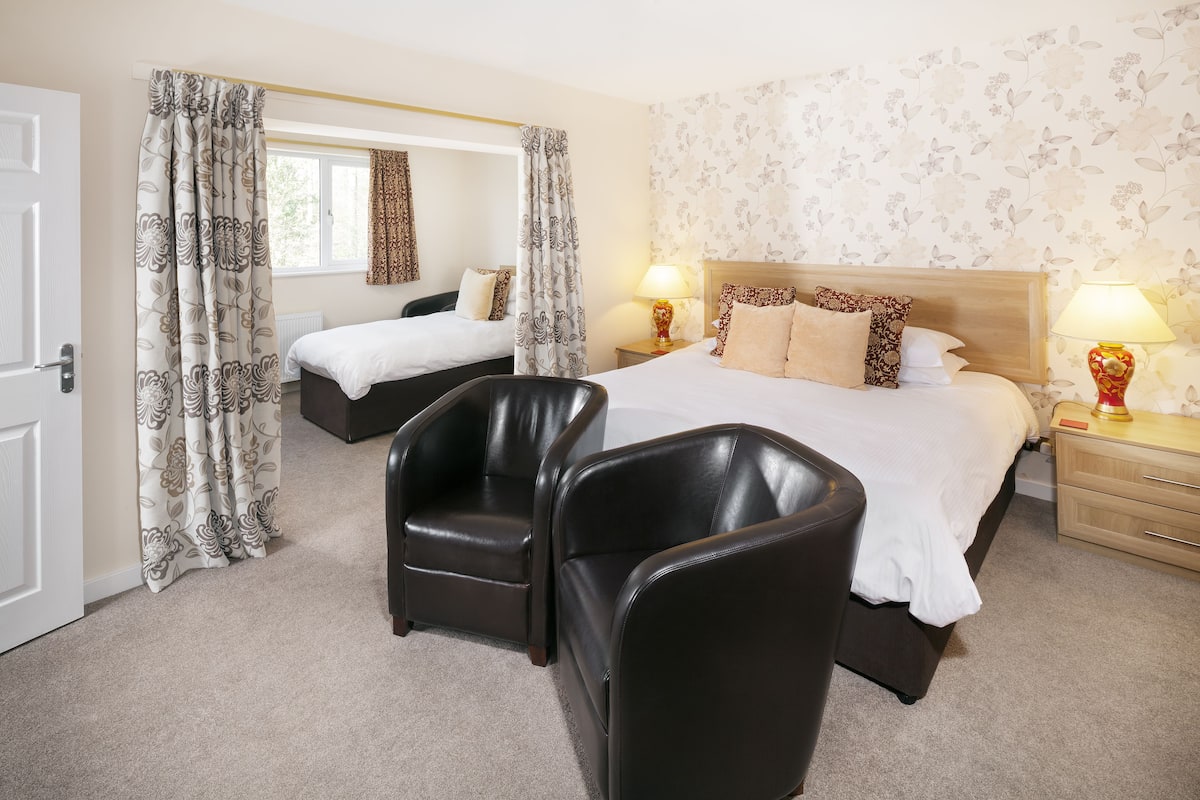 A hotel room with two beds, a sitting area with chairs, a wooden headboard, and a floral wallpaper.