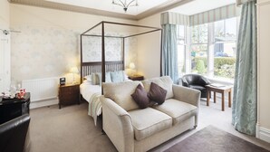 A bedroom with a four-poster bed, a sofa, a small table, and a chair.