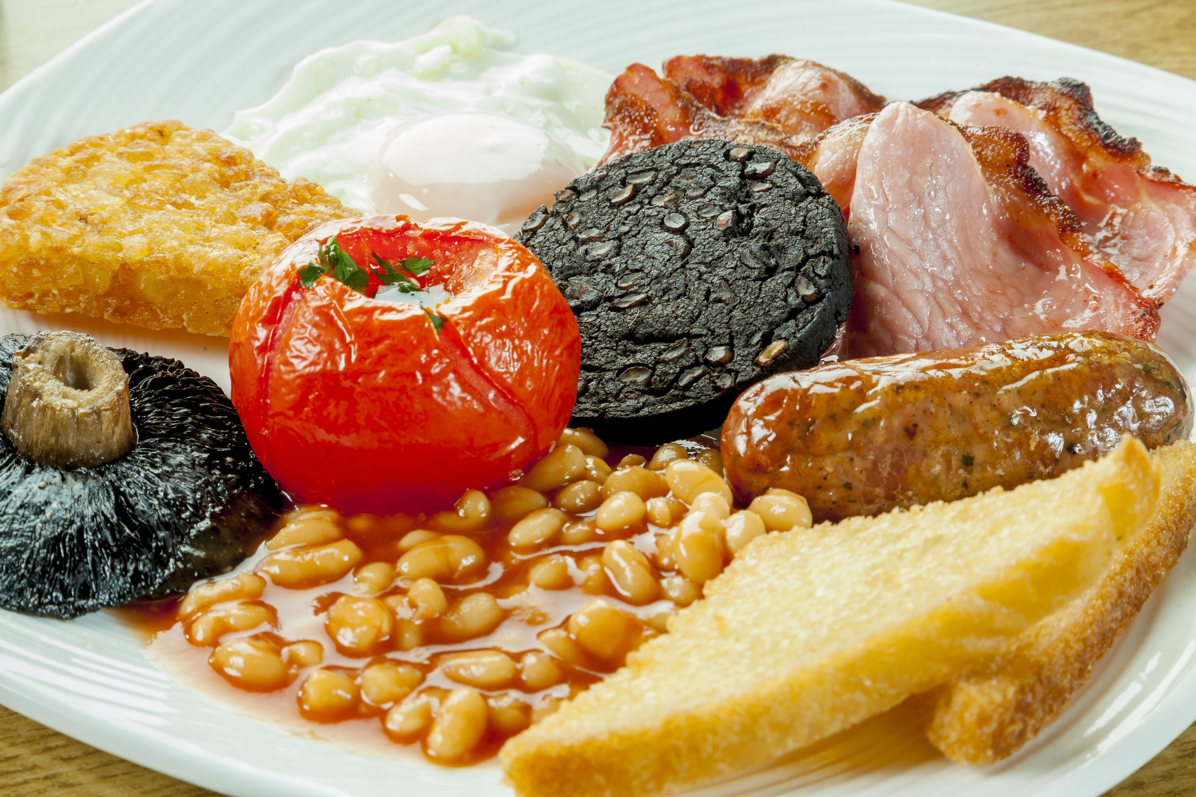 Un plato de comida para el desayuno con huevos, tocino, salchichas, frijoles, tostadas y tomate.