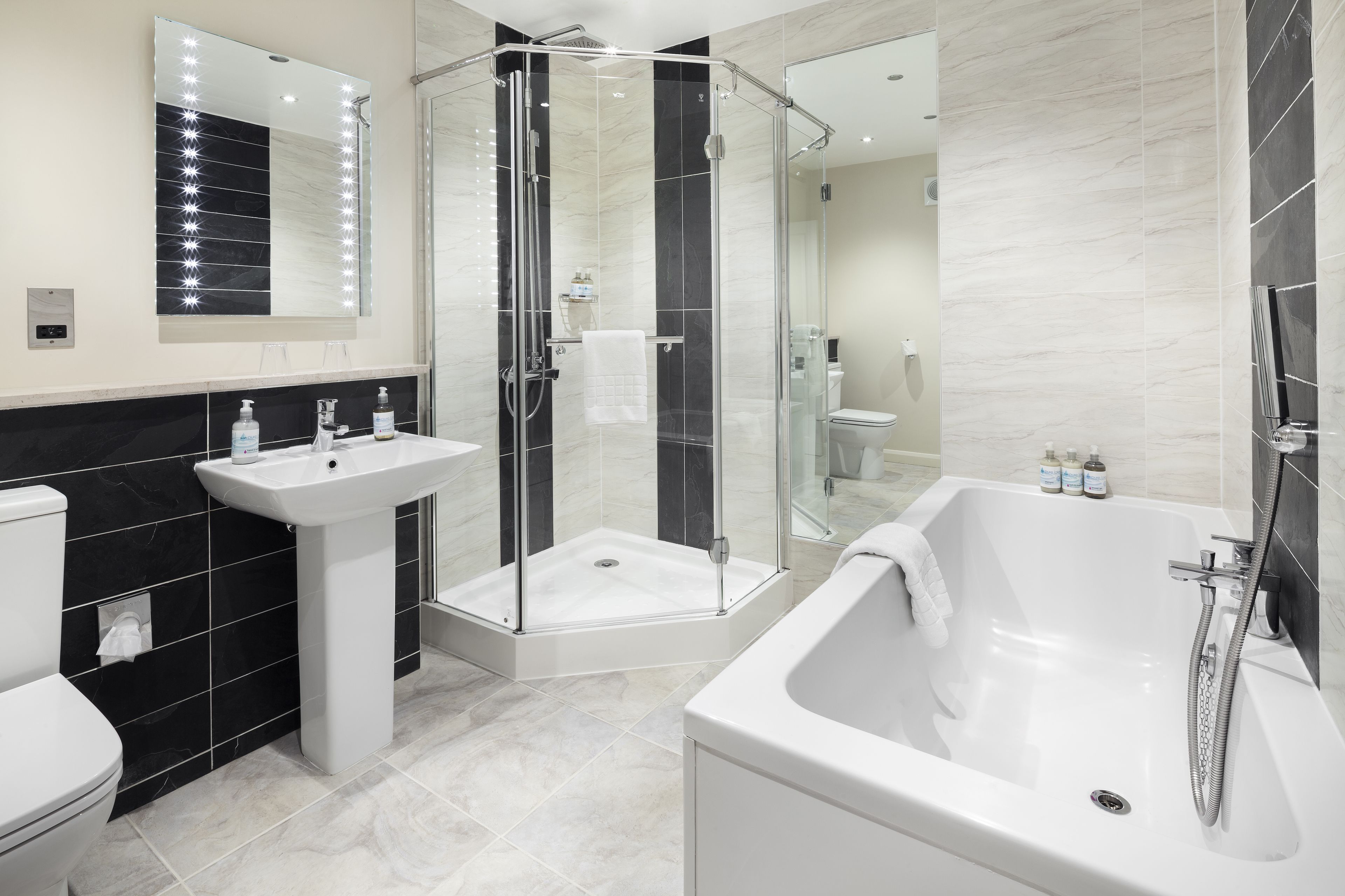 Un baño moderno con ducha envuelta en vidrio, una bañera grande y un tocador con espejo.