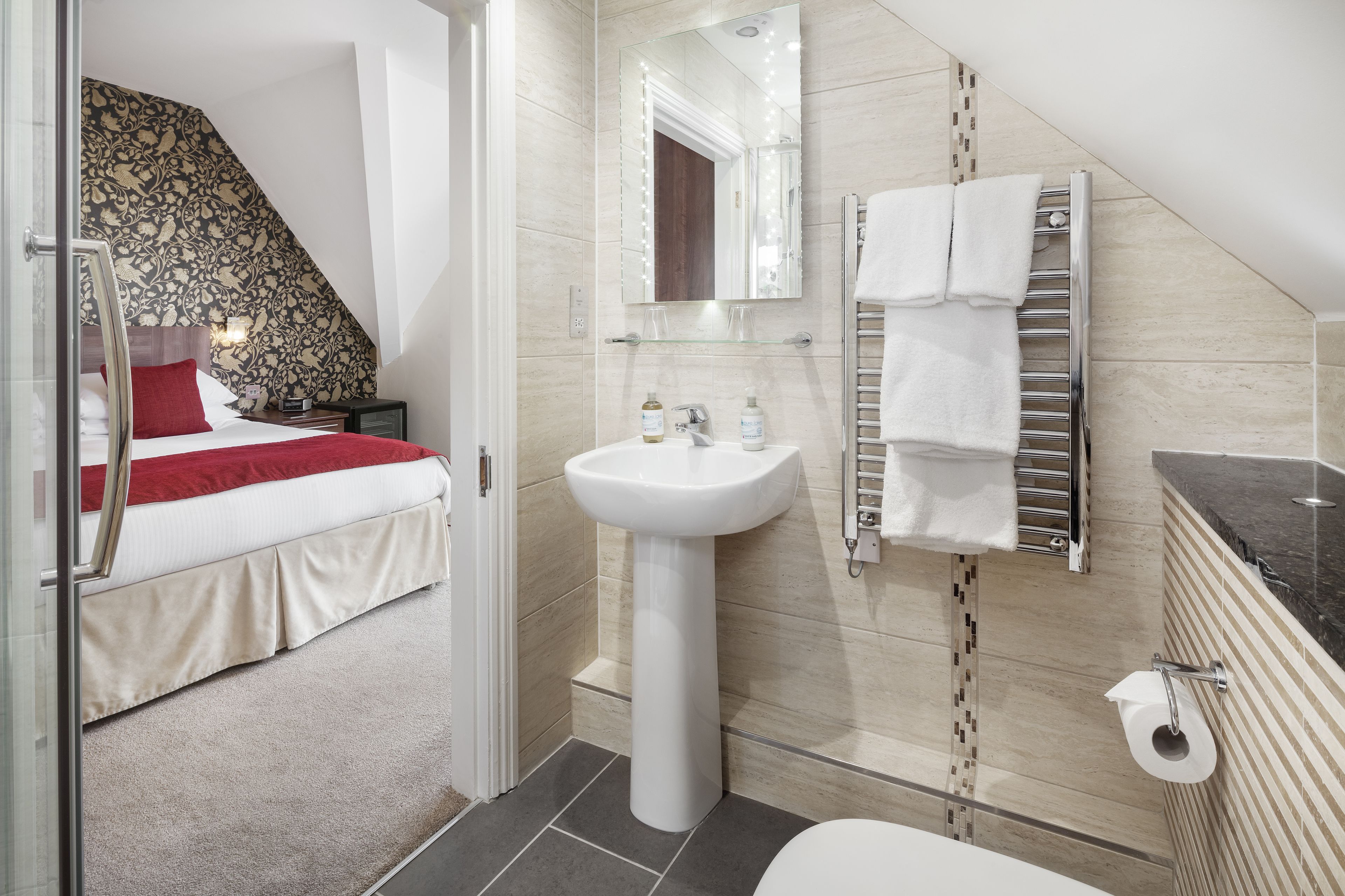 Un baño moderno con un lavamanos pedestal, estante de vidrio, toallero y un inodoro.