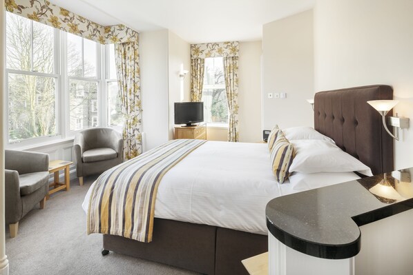 A hotel room with a bed, a TV, a chair, a desk, and large windows. - Hawksmoor Guest House (Windermere)