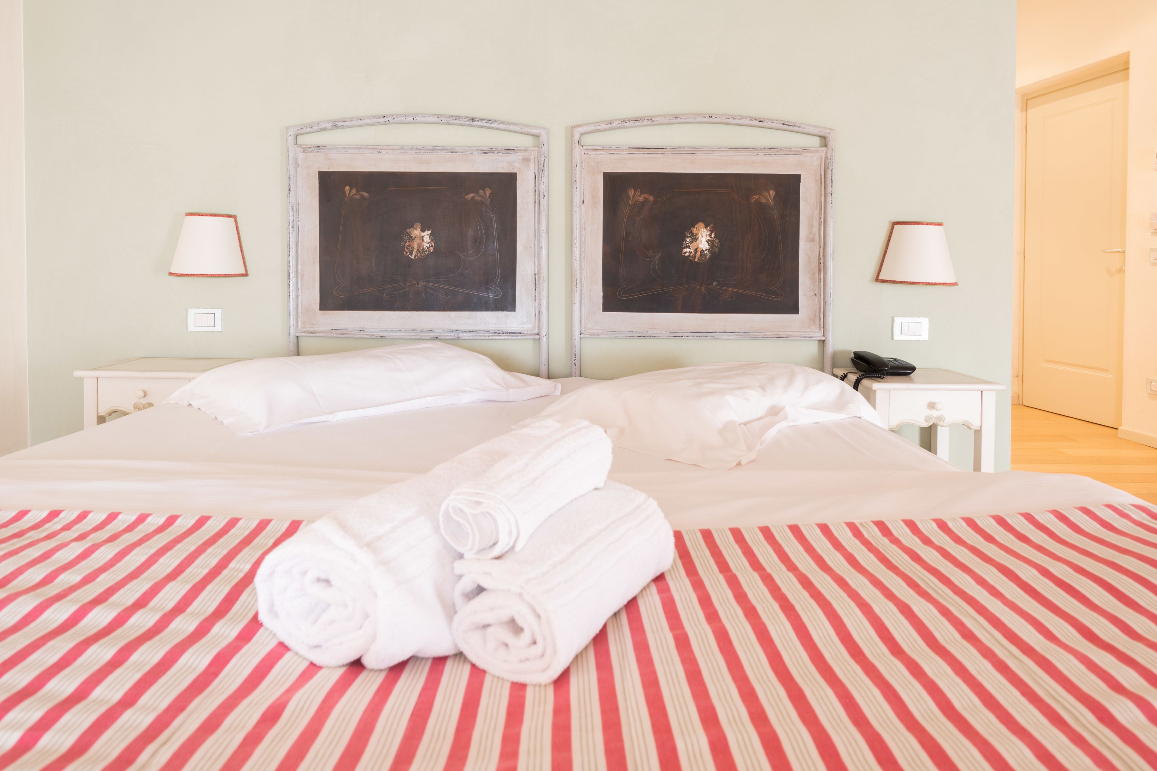 A double bed with a striped bedspread, two bedside tables with lamps, and two framed pictures on the headboard.