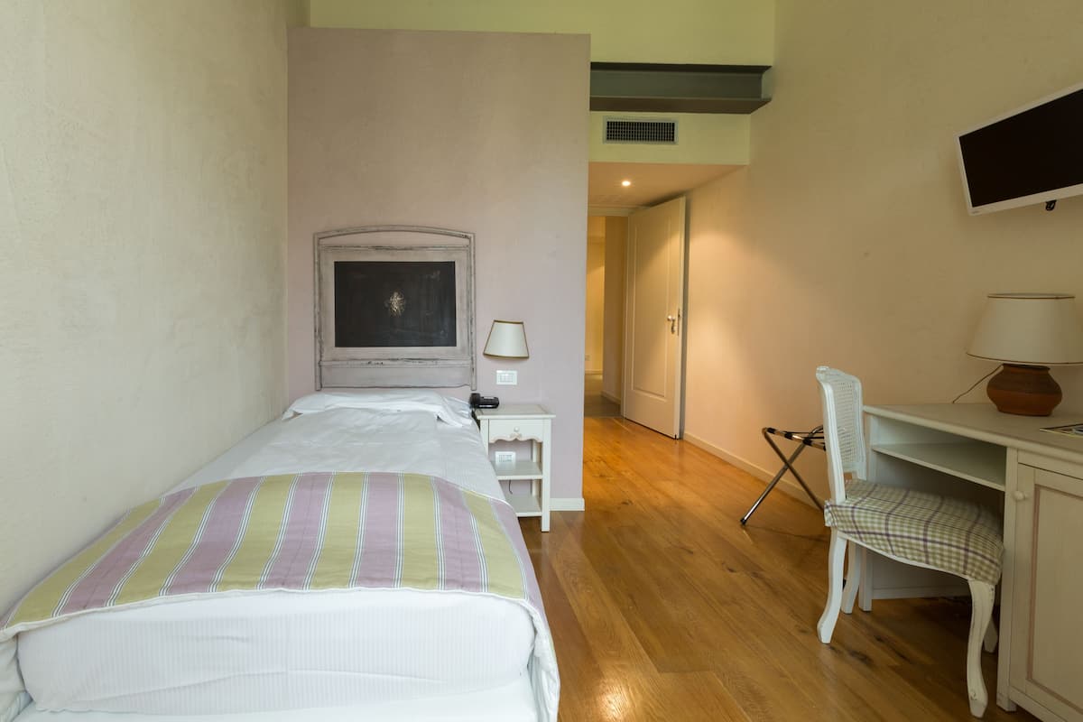 A hotel room with a bed, a desk with a chair, a television, and a lamp.
