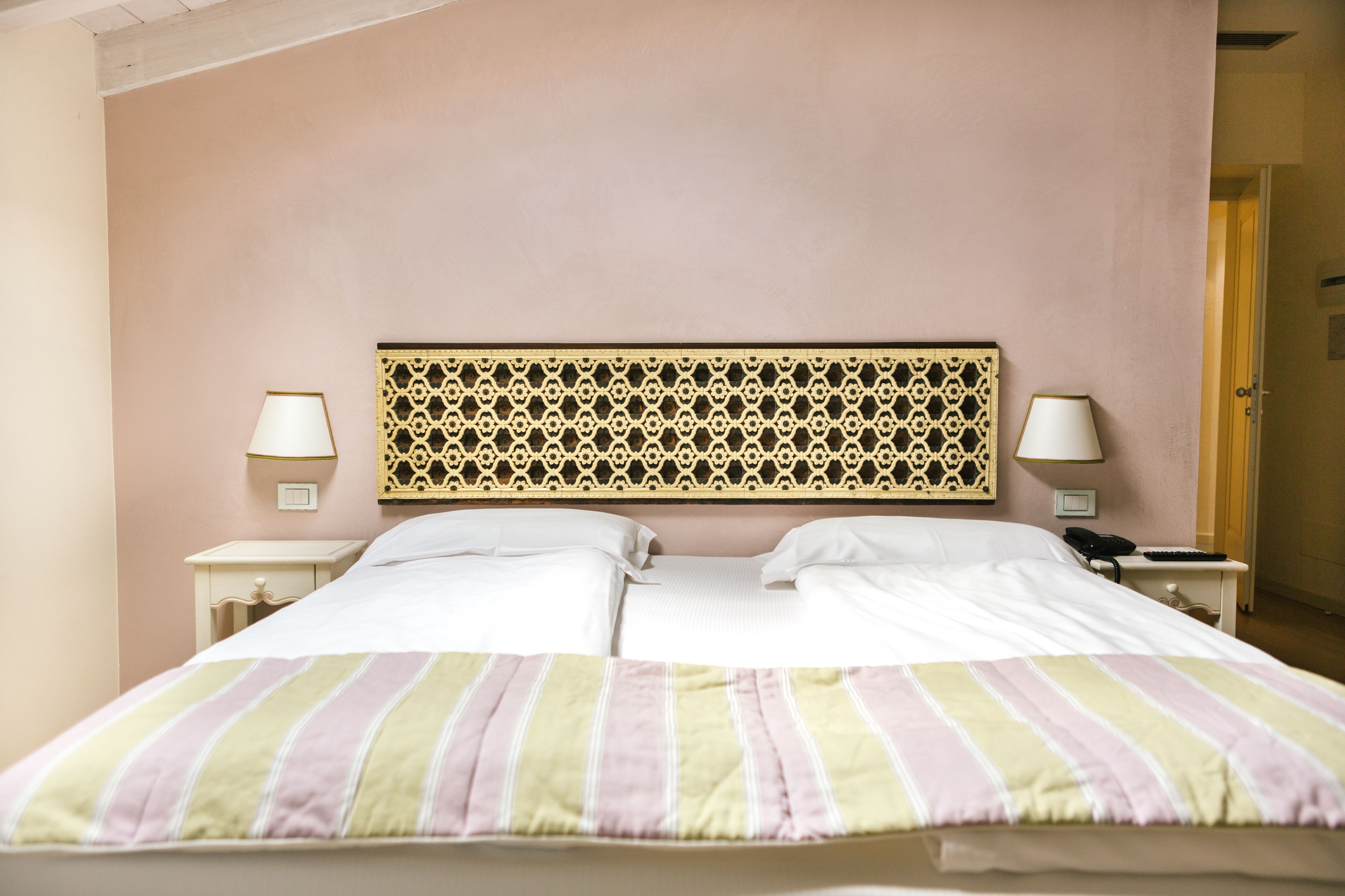 A double bed with a striped bedspread, two bedside tables with lamps, and a decorative headboard.