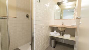 A bathroom with white tiled walls, a glass shower enclosure, a sink with a mirror above it, and a trash can.
